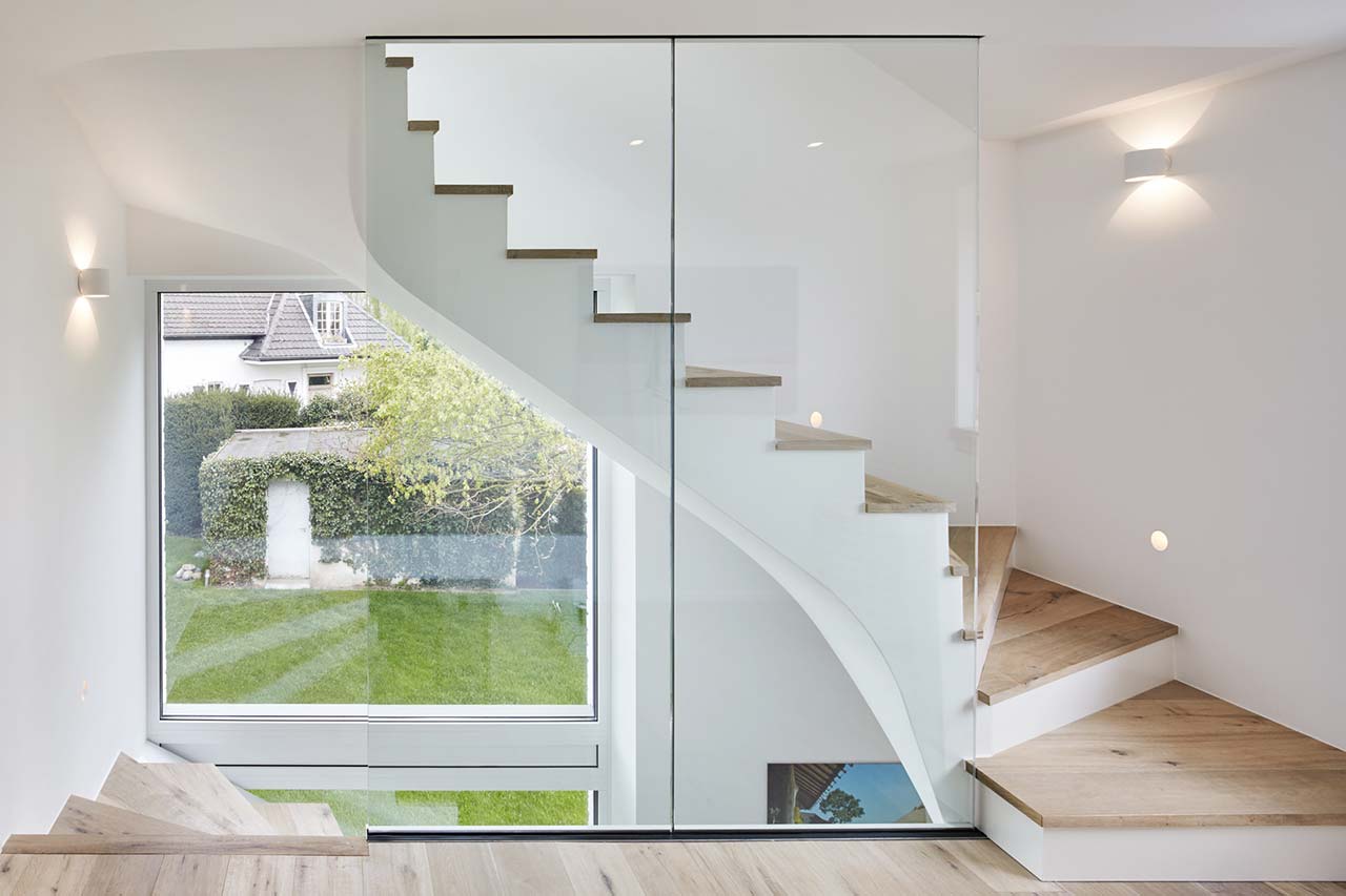 Treppenhaus mit Holzstufen und rahmenloser Glasplatte als Geländer.