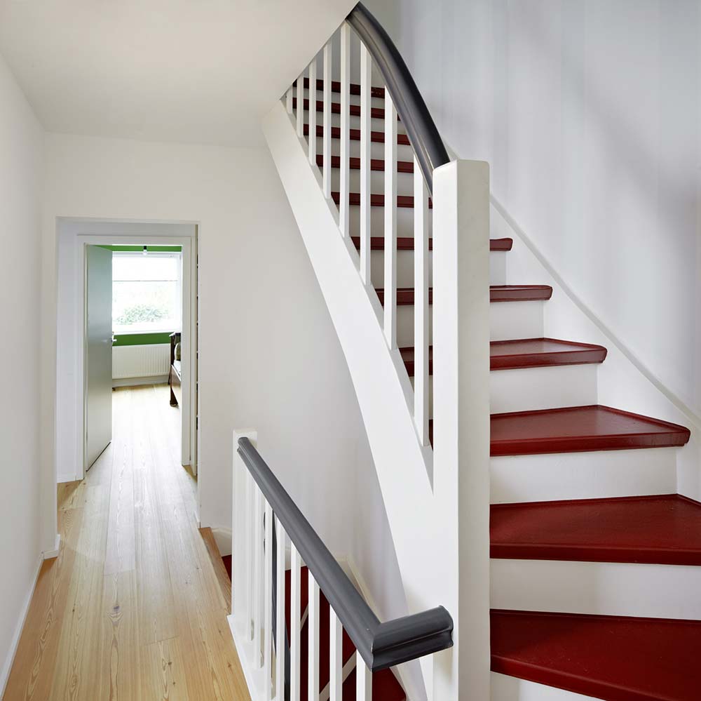 Weiß lackierte Treppe im sanierten Reihenendhaus aus den 20er Jahren mit roten Treppenstufen.