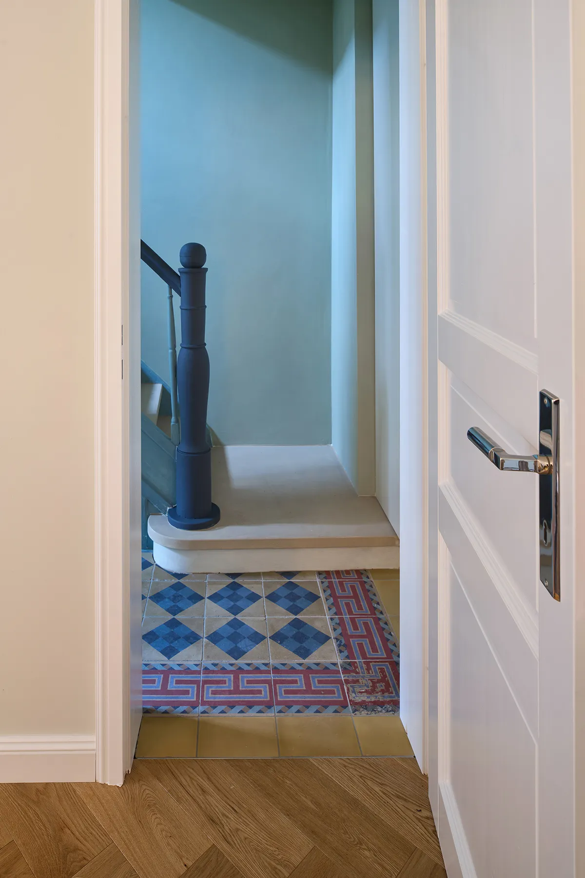 Blick vom Flur auf den sanierten Treppenaufgang mit historischem Fliesenboden und farbig gefasstem Geländer.