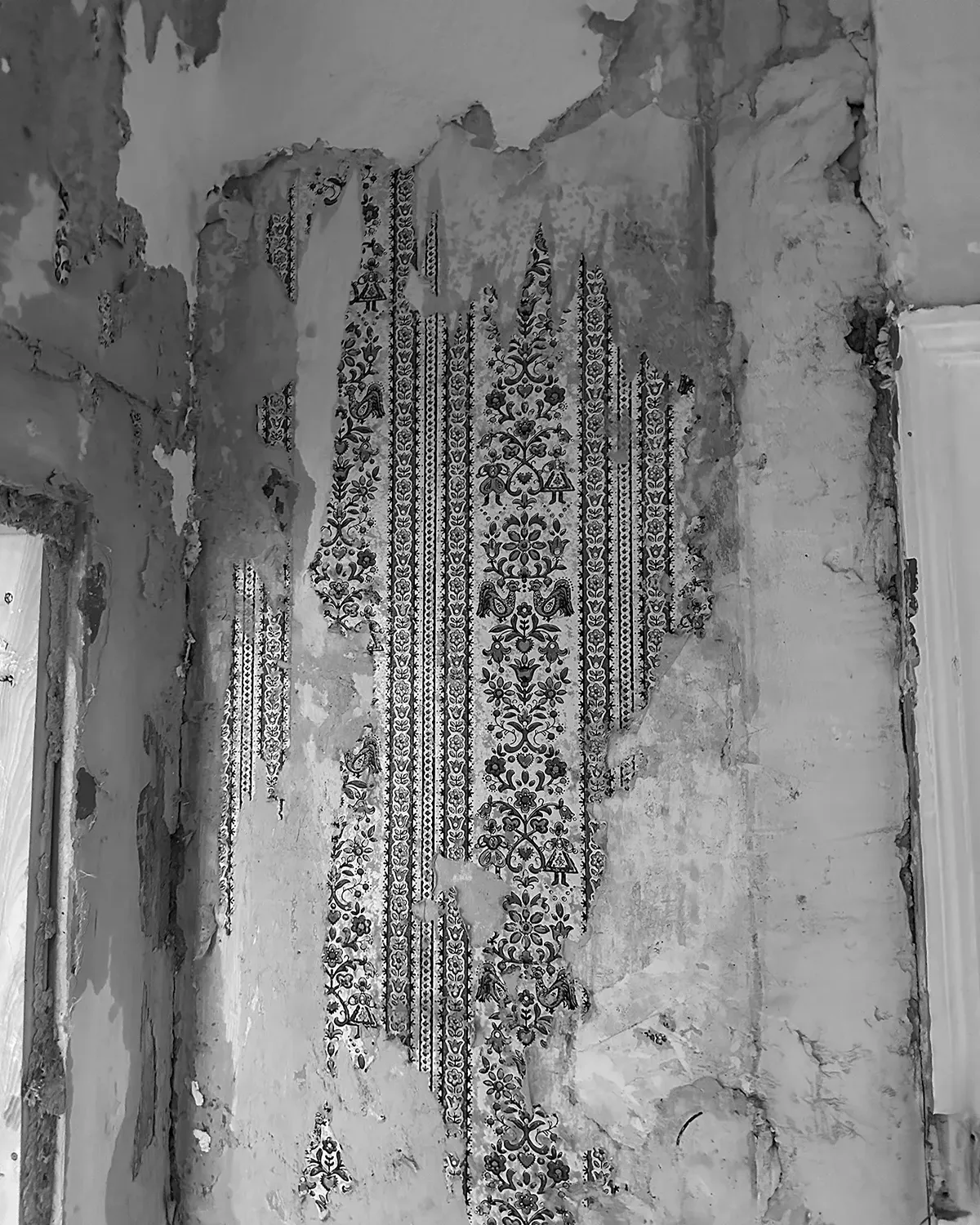 Freigelegte Wand während der Sanierung mit sichtbaren Resten historischer Tapete unter abplatzendem Putz.