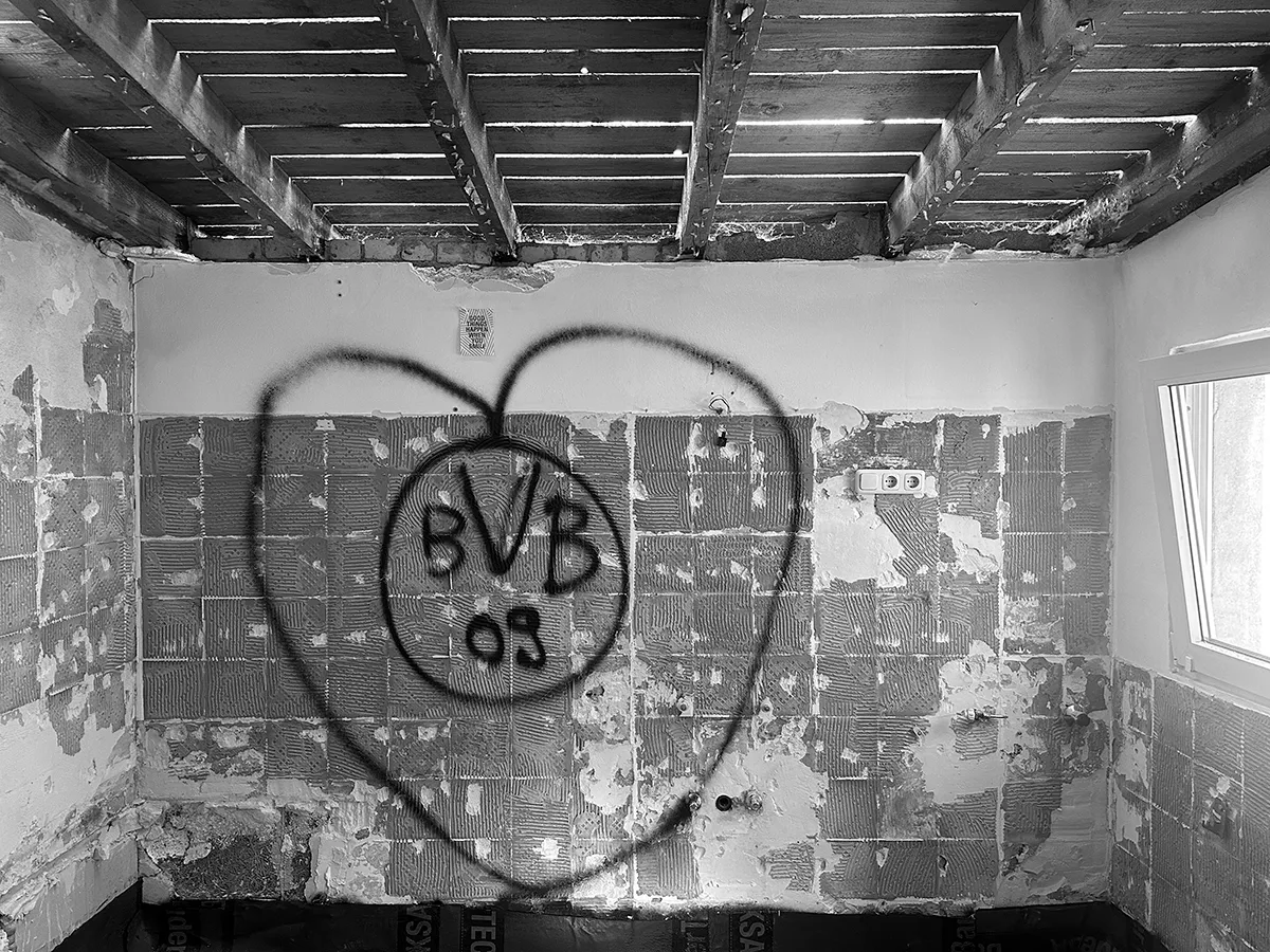 Raum während der Sanierung mit freigelegter Holzbalkendecke, rohem Mauerwerk und markierter Wandfläche.