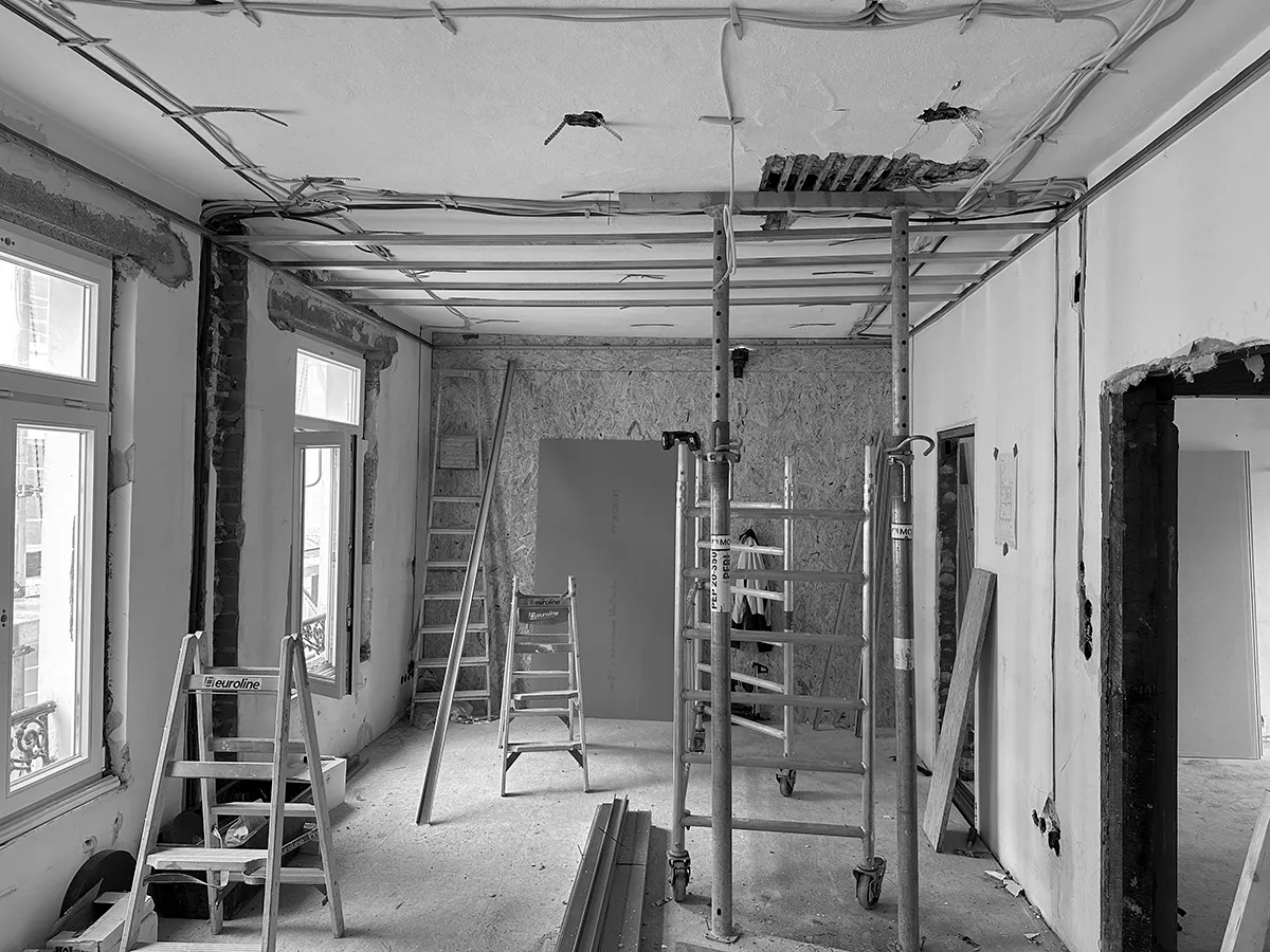 Innenraum während der Sanierung mit freigelegter Decke, sichtbarer Haustechnik, Gerüst und Baustellenmaterial.