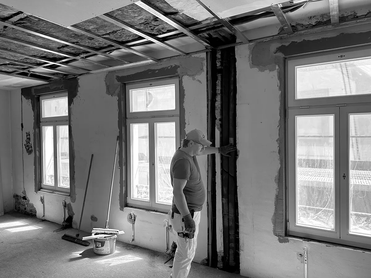 Innenraum während der Sanierung mit freigelegten Installationsschächten, geöffneten Wandflächen und sichtbarer Deckenkonstruktion.