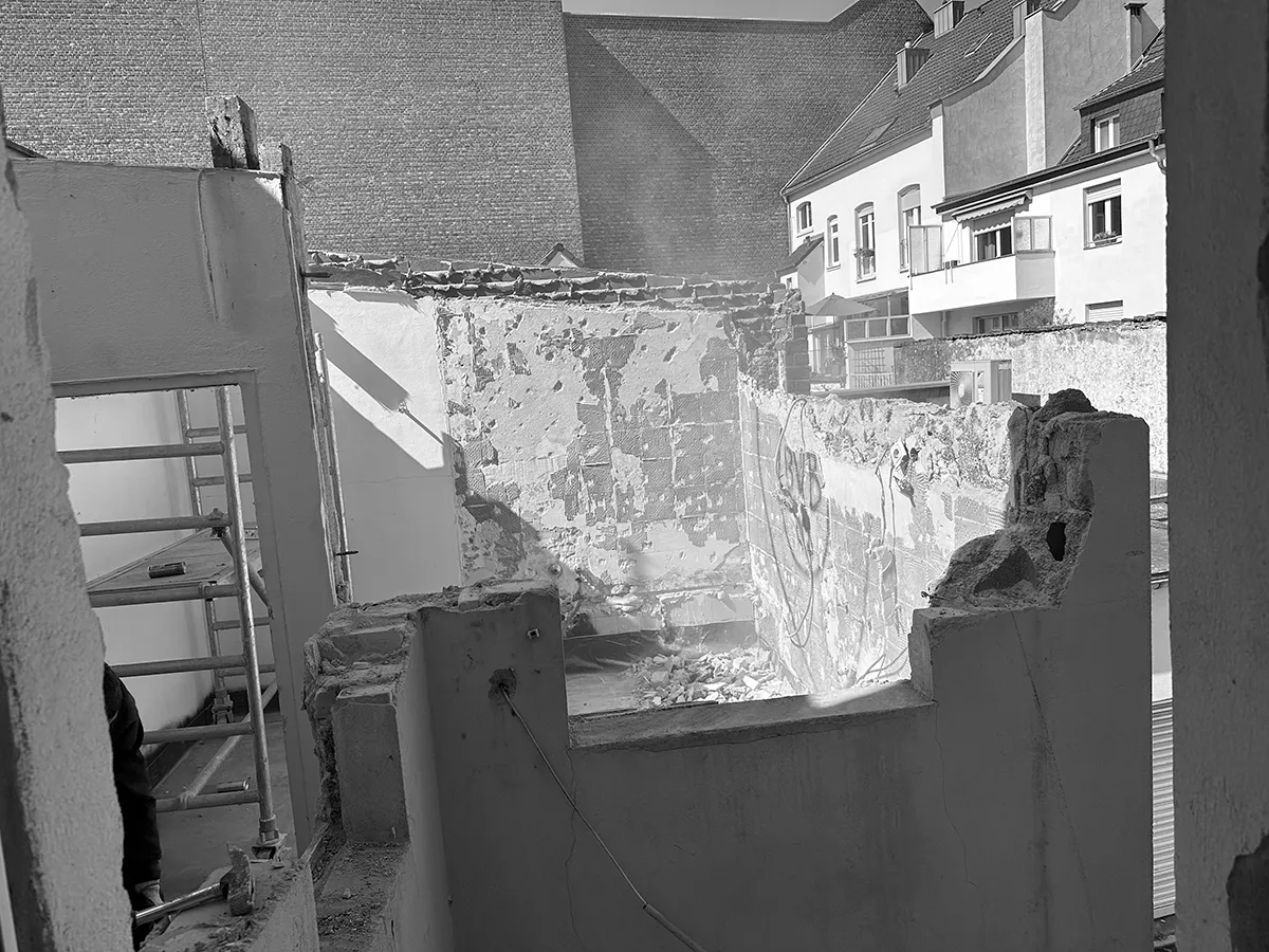 Außenwand während der Sanierung mit freigelegtem Mauerwerk, Teilabbruch und Blick auf die angrenzende Nachbarbebauung.