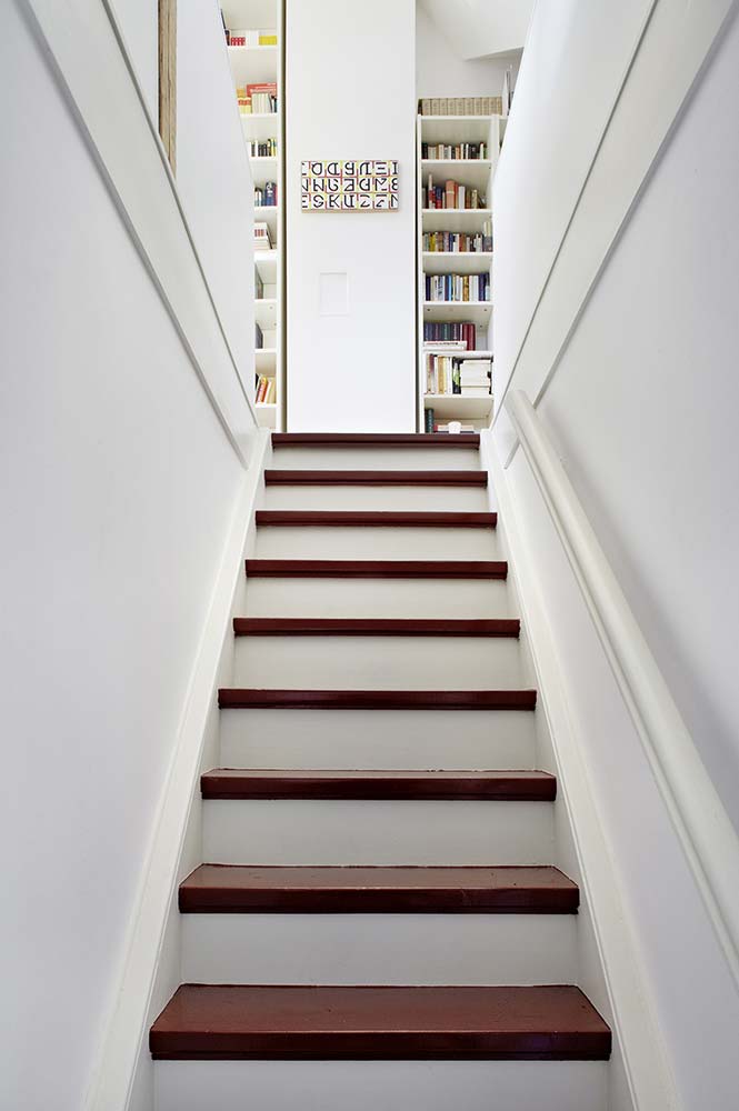 Sanierter Treppenaufgang in einem alten Haus, weiß lackiert mit roten Stufen.