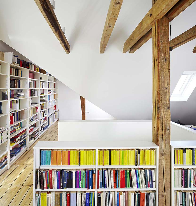 Bibliothek im Dachgeschoss eines modernisierten Hauses mit weißen Regalen und freiliegenden Holzbalken.