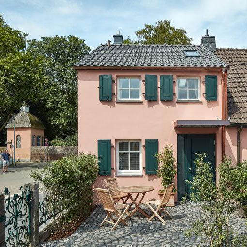 Ein kleines Dorfhaus in Düsseldorf Kalkum, saniert und umgebaut, mit rosa Fassade und kleinem Terrassenvorplatz.